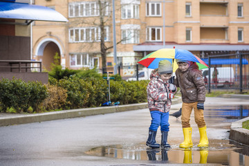 Two little boys, squat on a puddle, with little umbrellas