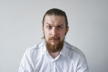 Headshot of displeased angry unshaven young employee staring at camera with grumpy and pissed off look, frowning, having bad mood, feeling dissatisfied and furious about something. Human emotions