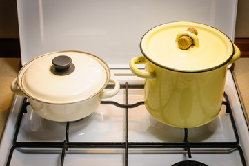 A yellow and a white pot on the gas stove in the kitchen