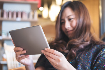 A beautiful Asian woman with smiley face holding and using tablet pc in modern cafe