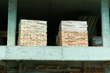 Building construction site with two pallets of the industrial bricks on the floor and concrete poles.