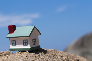 Toy houses standing on rock on background of the sky