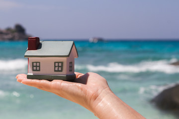 Toy houses keeps on hand against the blue sea.