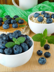 Blueberries in a ceramic bowl. Oatmeal and sandwich with peanut butter in the background 