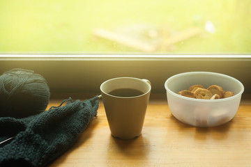 Obraz na płótnie Canvas Cozy home still life: cup of hot coffee, cookies, homemade knitting on windowsill. Spring or summer time concept, toned photo