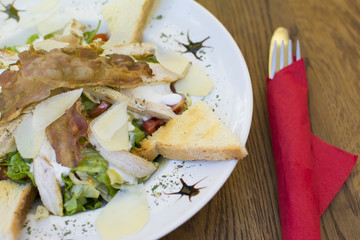 Delicious caesar salad with cheese on a rustic wooden table. Delicious meal in the restaurant on a sunny day.