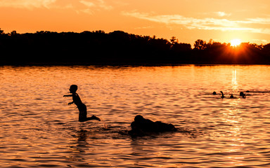 Naklejka na ściany i meble Kids and families are having fun at a lake under sunset