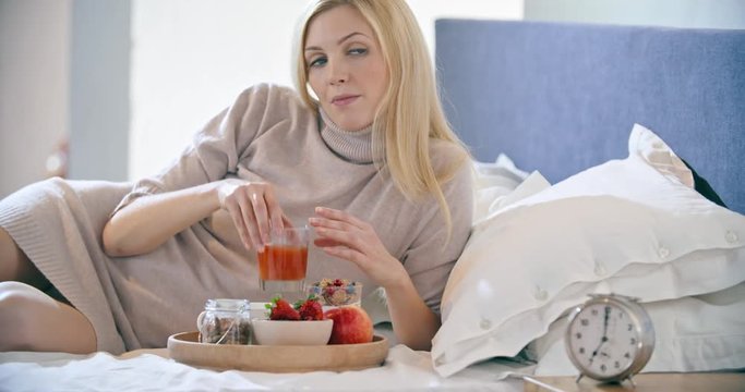 Beautiful woman eating breakfast with yogurt, fruit and cereals on bed. Morning wake up at home in bedroom. Caucasian people liying on bed. 4k video