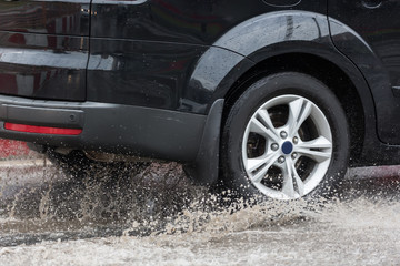 Car driving through a puddle on a flooded road with water and splashes caused by heavy rain.