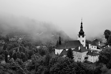 Summer in Slovakia. Old mining village. Historic church in Spania dolina. Black and white colored country in fog after the storm. - obrazy, fototapety, plakaty