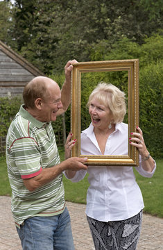 Elderly couple playing with a picture frame in a garden setting