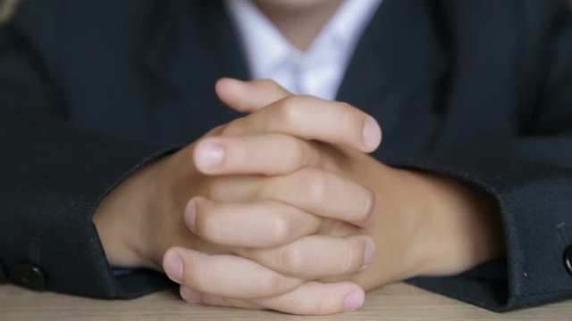 The boy touches his fingers while sitting at his desk