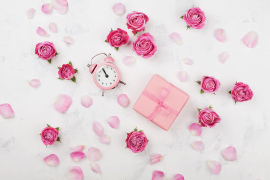 Gift box, alarm clock, petals and pink rose flowers on white table top view in flat lay style. Greeting for Mother or Woman day concept.