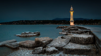 A wide angle shot of a lit lighthouse in Lake Geneva, Switzerland during early evening
