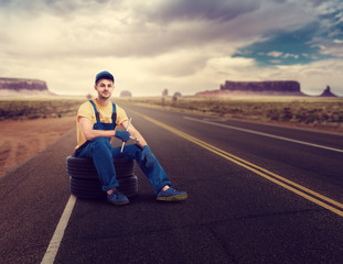 Service mechanic sitting on tire, desert road