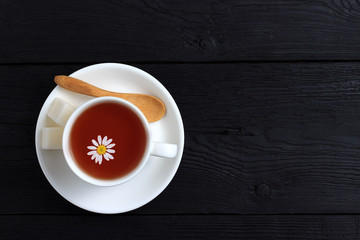 Tea with chamomile in a white cup on a black wooden background