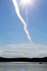 Trail from the plane, sun rays, boat on the lake