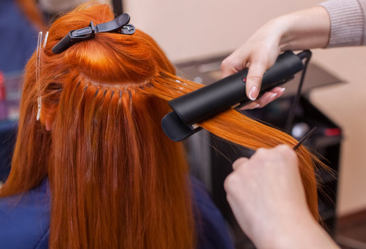 Hairdresser makes hairstyle girl with long red hair in a beauty salon. Straightening hair ironing. Professional hair care.