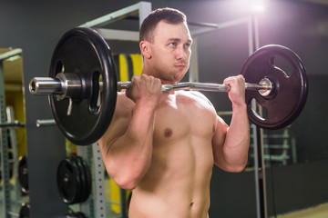 Fototapeta na wymiar Strong man - bodybuilder with dumbbells in a gym, exercising with a barbell.