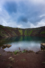 Fototapeta na wymiar Iceland - Red dusty ground before clear blue water at Kerid Crater Lake