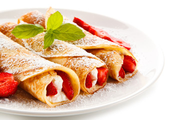 Crepes with strawberries and cream on white background