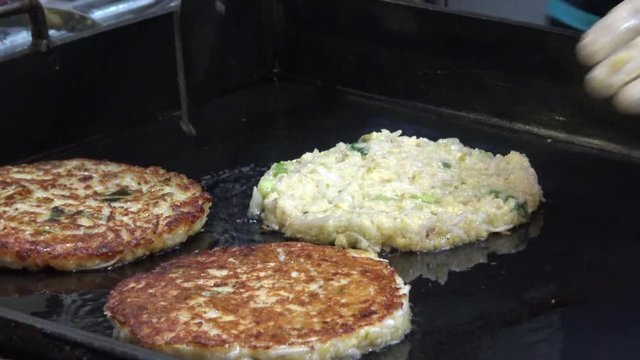 4K Bindae-tteok in Gukje International Market Busan city. Bindaetteok, fried buchimgae, savory pancake with ground mung beans, vegetables, meat. Korean vendors selling food in street, South Korea-Dan