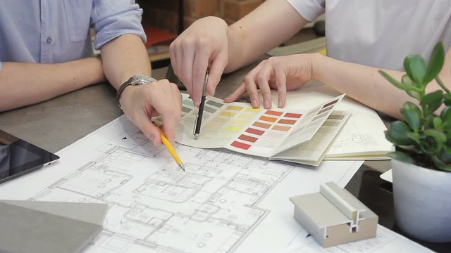 Two people above the drawing room choose the color for the interior. Creative team come up with an unusual design for the house. Designers are working on projects.