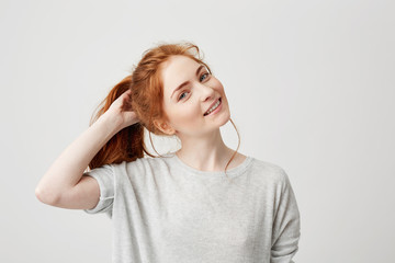 Fototapeta premium Portrait of young cute redhead girl smiling looking at camera touching hair over white background.