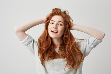 Portrait of happy young beautiful redhead girl smiling looking at camera touching hair over white background.