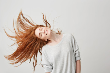 Portrait of young cheerful beautiful redhead girl smiling with closed eyes shaking head and hair over white background.