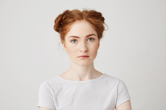 Close up photo of young beautiful ginger girl with buns looking at camera over white background.