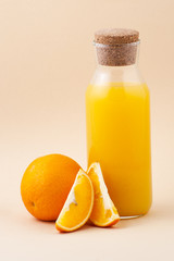 Fresh orange juice in a glass bottle and orange on a light beige background..