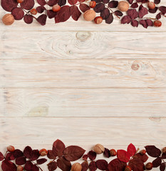 Flat lay frame of autumn crimson leaves, hazelnuts and walnuts on a light wooden background.