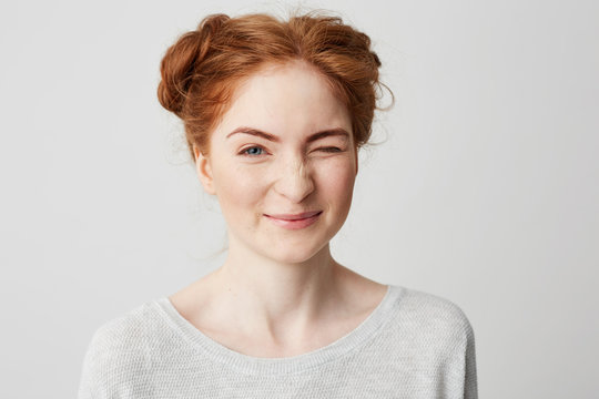 Close up of young cute redhead girl smiling looking at camera winking over white background.