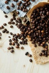 Roasted coffee beans scattered from paper bag over dark gray granite plate, captured from top view with sharp focus