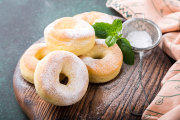 Homemade baked donuts with powdered sugar on green background. Selective focus.