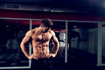Fototapeta na wymiar Handsome bodybuilder is standing in the modern gym.