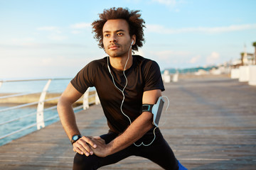 Fit male Afro-American jogger with bushy hairstyle warming-up his muscles before running. Man...