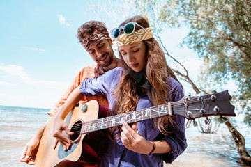 Fototapeta na wymiar Beautiful young couple in love in hippie style with the guitar resting on the beach in summer. A Girl holding a guitar, man teaches how to play his girlfriend on the seafront
