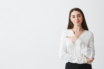 Young beautiful brunette businesswoman smiling looking at camera pointing finger in side over white background.