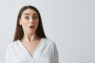 Portrait of surprised young beautiful businesswoman looking at camera with opened mouth over white background.