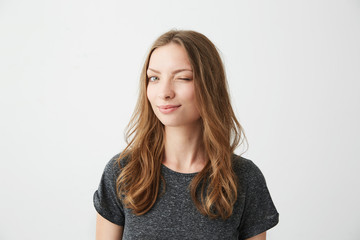 Obraz premium Portrait of young positive girl smiling winking looking at camera over white background.