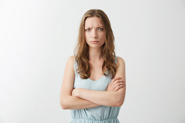 Fototapeta premium Offended displeased young girl frowning looking at camera with crossed arms over white background.