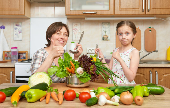 Mother and daughter cook and taste soup from vegetables. Home kitchen interior. Parent and child, woman and girl. Healthy food concept