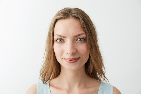 Close up portrait of young beautiful blonde girl with blue eyes smiling looking at camera over white background.