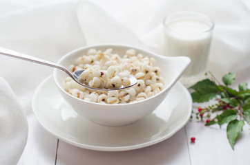 Healthy breakfast with boiled job's tears porridge in white bowl and spoon on wooden table.