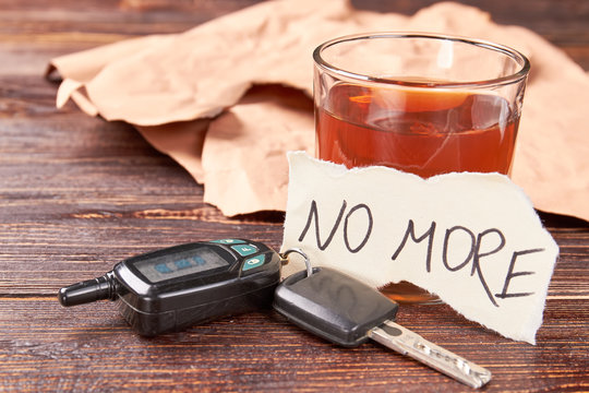 Booze in glass, car keys, paper message. Message no more, alcohol in glass, car keys on wooden background. Automobile accidents and abuse of alcohol.