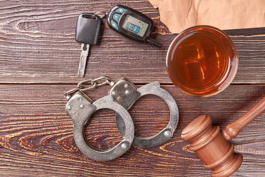 Gavel, key, handcuffs, whiskey, top view. Handcuffs, gavel, glass of whiskey, driving keys on wooden background.
