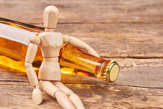 Human wooden dummy hugs bottle. Human wooden figure, closed alcoholic beverage, wooden background.
