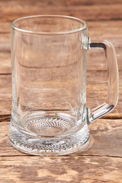 Empty beer mug isolated on wooden background. Transparent glass container for beer, old wooden table.